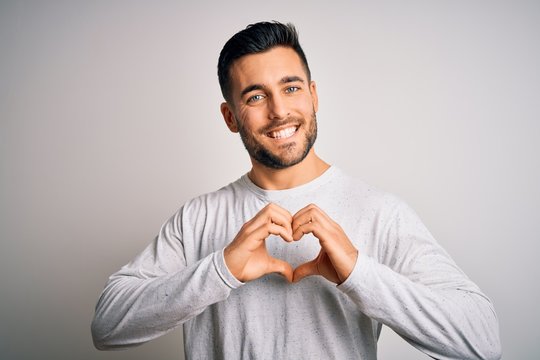 Young handsome man wearing casual t-shirt standing over isolated white background smiling in love showing heart symbol and shape with hands. Romantic concept.