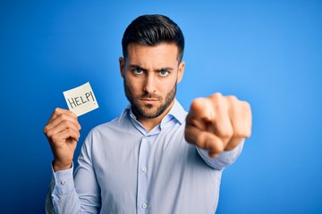 Young overworked business man asking for help holding paper over blue background pointing with...