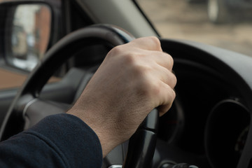 Man's hand holding the steering wheel of a car close-up
