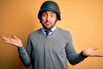 Young handsome businessman wearing military helmet over isolated yellow background clueless and...