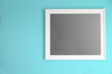 White empty photo frame hanging on turquoise color wall