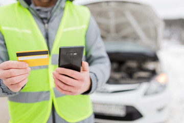 Close up of man using mobile phone and roadside assistance insurance membership card next to broken car.