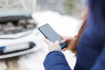 Transportation, vehicle and winter concept. Woman using blank screen mobile phone call or texting car mechanic road assistance service.