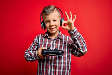 Young little caucasian gamer kid playing video games using gamepad joystick over red background...