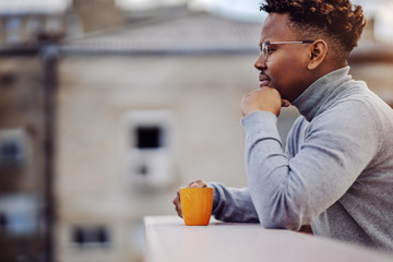Side view of attractive african american man leaning, holding mug with fresh coffee and daydreaming.