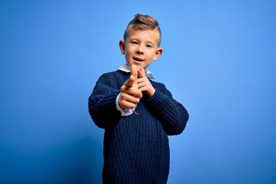 Young little caucasian kid with blue eyes wearing winter sweater over blue background pointing fingers to camera with happy and funny face. Good energy and vibes.