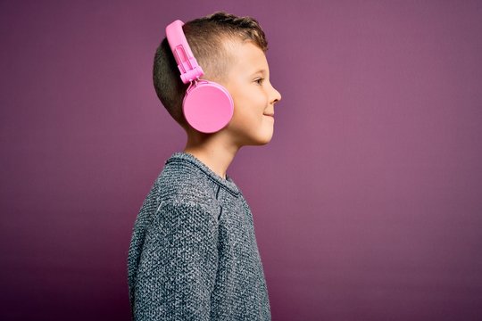 Young little caucasian kid wearing headphones listening to music over purple background looking to side, relax profile pose with natural face with confident smile.