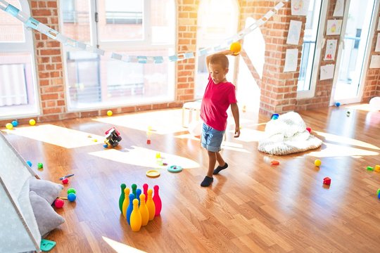 Adorable toddler playing bowling around lots of toys at kindergarten