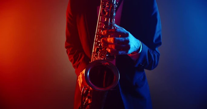 Saxophonist wearing a suit performing a solo on stage with band, spotted by red and blue lights of club - music, art concept 4k footage