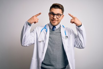 Young doctor man with blue eyes wearing medical coat and stethoscope over isolated background smiling pointing to head with both hands finger, great idea or thought, good memory