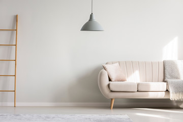 Pillow and blanket on elegant sofa in spacious living room with copy space wall