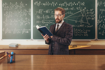 Bearded professor in suit and glasses citing a manual to explain the math lecture material