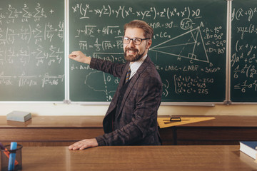 Cheerful bearded professor in glasses explaining the formulas he has written on a chalkboard
