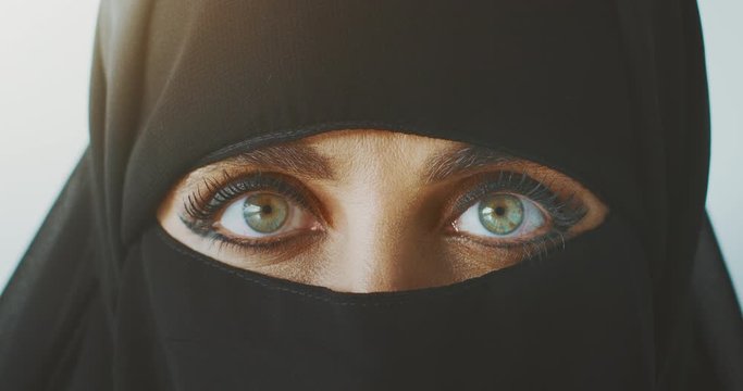 Portrait of a muslim woman wearing traditional black niqab showing only her green eyes, middle east culture