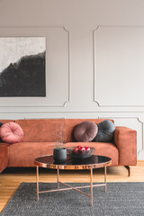 Flowers in vase and red fruits in bowl on wooden coffee table in elegant living room interior with...