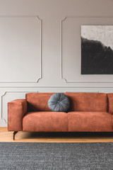 Vertical view of stylish ginger sofa with grey round pillow in sophisticated living room interior