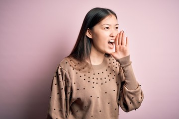 Young beautiful asian woman wearing fashion and elegant sweater over pink solated background shouting and screaming loud to side with hand on mouth. Communication concept.