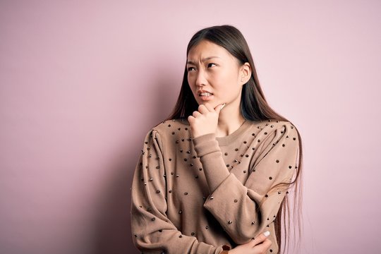 Young beautiful asian woman wearing fashion and elegant sweater over pink solated background Thinking worried about a question, concerned and nervous with hand on chin