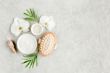 Fototapeta na wymiar Spa treatment concept. Natural/Organic spa cosmetics products, sea salt, massage brush, tropic palm leaves on gray marble table from above. Spa background with a space for a text, flat lay, top view