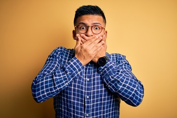 Obraz premium Young handsome latin man wearing casual shirt and glasses over yellow background shocked covering mouth with hands for mistake. Secret concept.