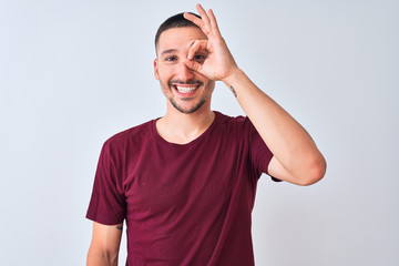 Young handsome man standing over isolated background doing ok gesture with hand smiling, eye looking through fingers with happy face.