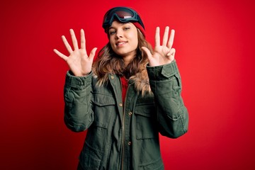 Young blonde girl wearing ski glasses and winter coat for ski weather over red background showing and pointing up with fingers number nine while smiling confident and happy.