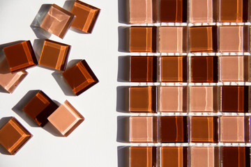glass mosaic tiles of coffee shades: beige, chocolate, brown on a white background and its individual square elements located on the side of the main glued part in sunlight with highlights