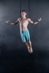 Fototapeta na wymiar Circus artist on the aerial straps with Strong muscles on black background wearing casual clothes 