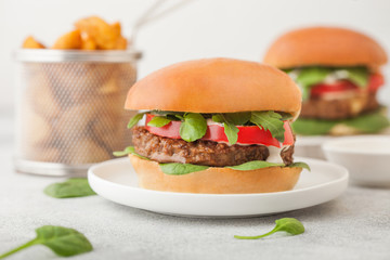 Healthy vegetarian meat free burgers on round ceramic plate with vegetables on light table background with potato wedges.