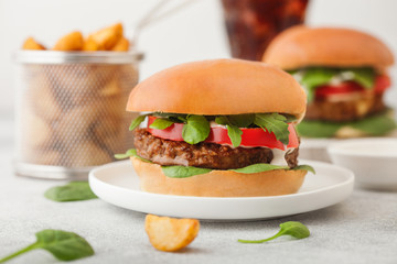 Healthy vegetarian meat free burgers on round ceramic plate with vegetables on light table background with potato wedges and glass of cola.