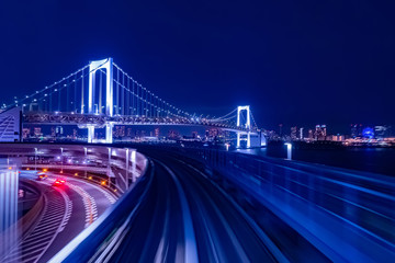 Japan. Evening panorama of Tokyo in blue. Life in the big city. Railway and road tracks on the background of the Rainbow bridge. Cars go on the highway in Tokyo. Rainbow bridge and Odaiba.