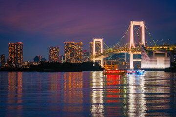 Fototapeta na wymiar Japan. Evening in Tokyo. View of Tokyo Bay from the shore. Pleasure ships on the background of the Rainbow bridge. Panorama of the Rainbow bridge and Odaiba island. The evening lights of Tokyo.