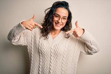 Beautiful woman with curly hair wearing casual sweater and glasses over white background looking...