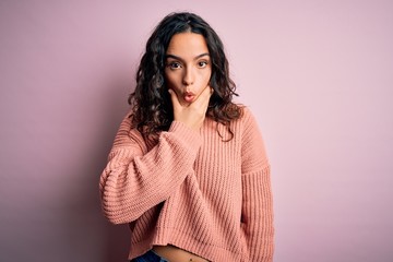 Young beautiful woman with curly hair wearing casual sweater over isolated pink background Looking fascinated with disbelief, surprise and amazed expression with hands on chin