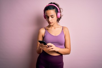 Sportswoman with curly hair doing sport listening to music using smartphone and headphones with a confident expression on smart face thinking serious