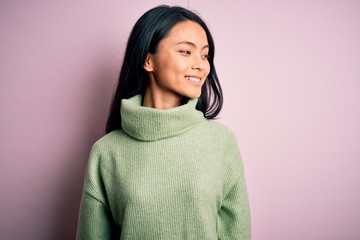 Young beautiful chinese woman wearing turtleneck sweater over isolated pink background looking away to side with smile on face, natural expression. Laughing confident.