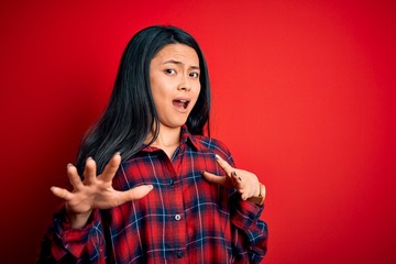 Young beautiful chinese woman wearing casual shirt over isolated red background afraid and terrified with fear expression stop gesture with hands, shouting in shock. Panic concept.