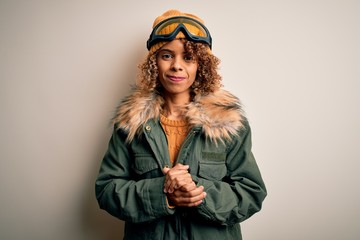 Young african american skier woman with curly hair wearing snow sportswear and ski goggles with hands together and crossed fingers smiling relaxed and cheerful. Success and optimistic