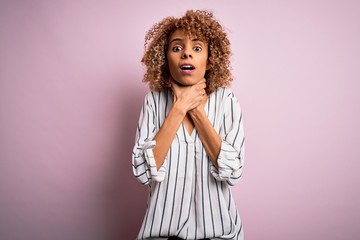 Beautiful african american woman with curly hair wearing striped t-shirt over pink background shouting and suffocate because painful strangle. Health problem. Asphyxiate and suicide concept.