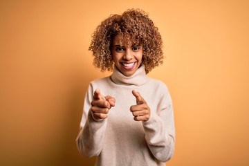 Young beautiful african american woman wearing turtleneck sweater over yellow background pointing fingers to camera with happy and funny face. Good energy and vibes.