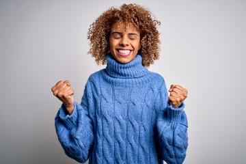 Young beautiful african american woman wearing turtleneck sweater over white background very happy and excited doing winner gesture with arms raised, smiling and screaming for success. Celebration