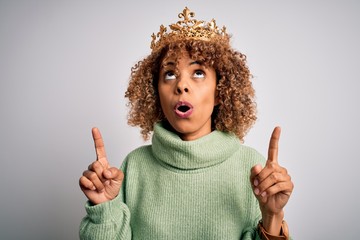 Young african american woman wearing golden crown of queen over isolated white background amazed...