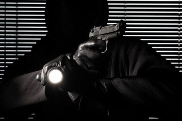 burglary and robbery. skillful professional masked burglar holding a gun and torch and breaking...