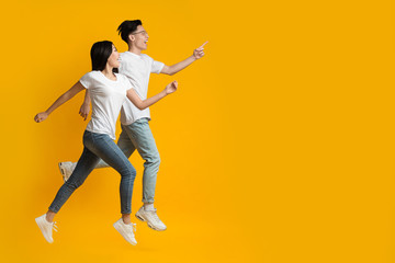Excited asian couple running towards copy space