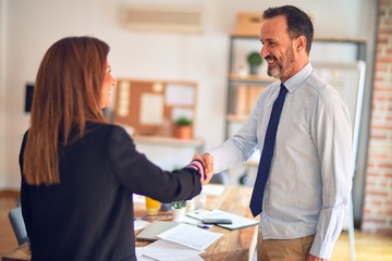 Two middle age business workers smiling happy and confident. Working together with smile on face doing handsake at the office