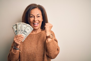Middle age brunette woman holding one dollars bank notes over isolated background screaming proud...