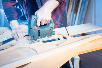 A man works with an electric jigsaw. Carpenter saws wood in the workshop. Carpenter's hands with electric jigsaw close-up. Woodworking tool. The sawing of wood.