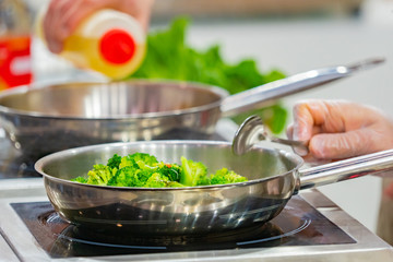 Restaurant kitchen. Cooking broccoli. Cook broccoli fry in a pan. Stainless steel kitchen utensils. Cook's job. Vegetable garnish. Vegetarianism. Frying pan with cabbage closeup.