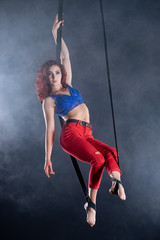 Female athletic, sexy and flexible aerial circus artist with redhead on aerial straps on black...