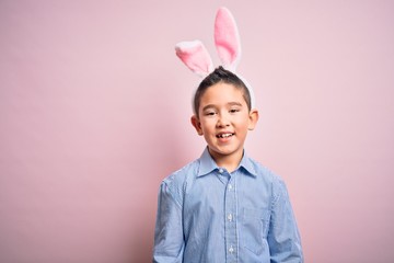 Young little boy kid wearing easter bunny ears over isolated pink background with a happy and cool smile on face. Lucky person.